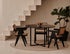 A round oak dining table with a charcoal finish and cross metal frame, featuring a smooth tabletop and modern design.