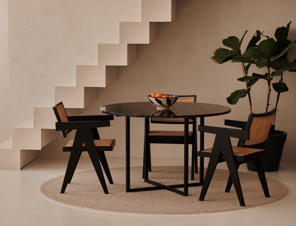 A round oak dining table with a charcoal finish and cross metal frame, featuring a smooth tabletop and modern design.