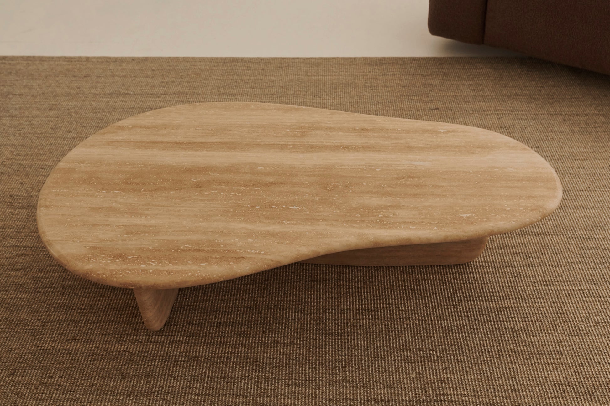 Form coffee table with a travertine top and sleek metal legs, showcasing a modern design in a living room setting.