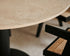 KIYO round dining table with travertine surface and black center-leg, showing slight side damage and small stains.