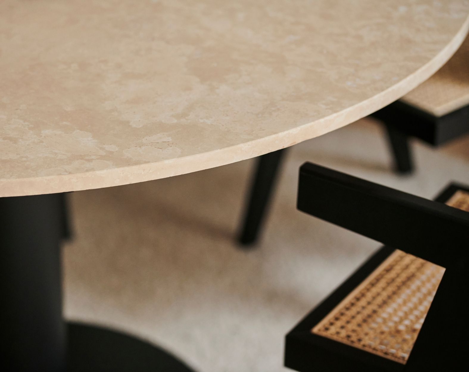 KIYO round dining table with travertine surface and black center-leg, showing slight side damage and small stains.