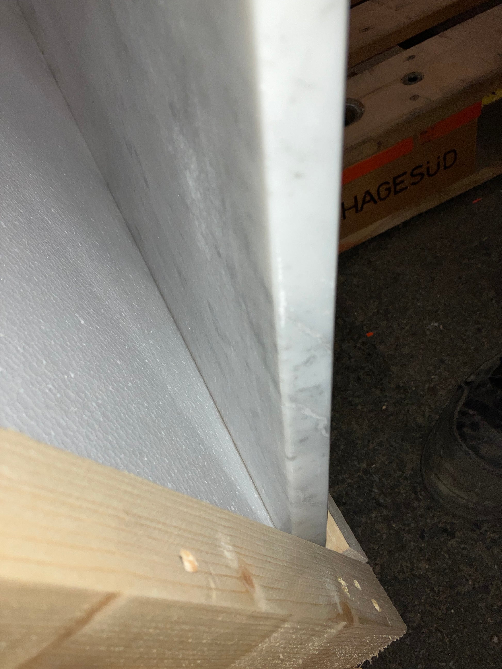 Rectangular marble dining table with white Bianco Carrara marble surface, four legs, matte gray finish, slight edge damage visible.