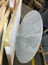 Oval marble dining table with Bianco Carrara white surface and cross-frame design, matte grey tint with small scratches.
