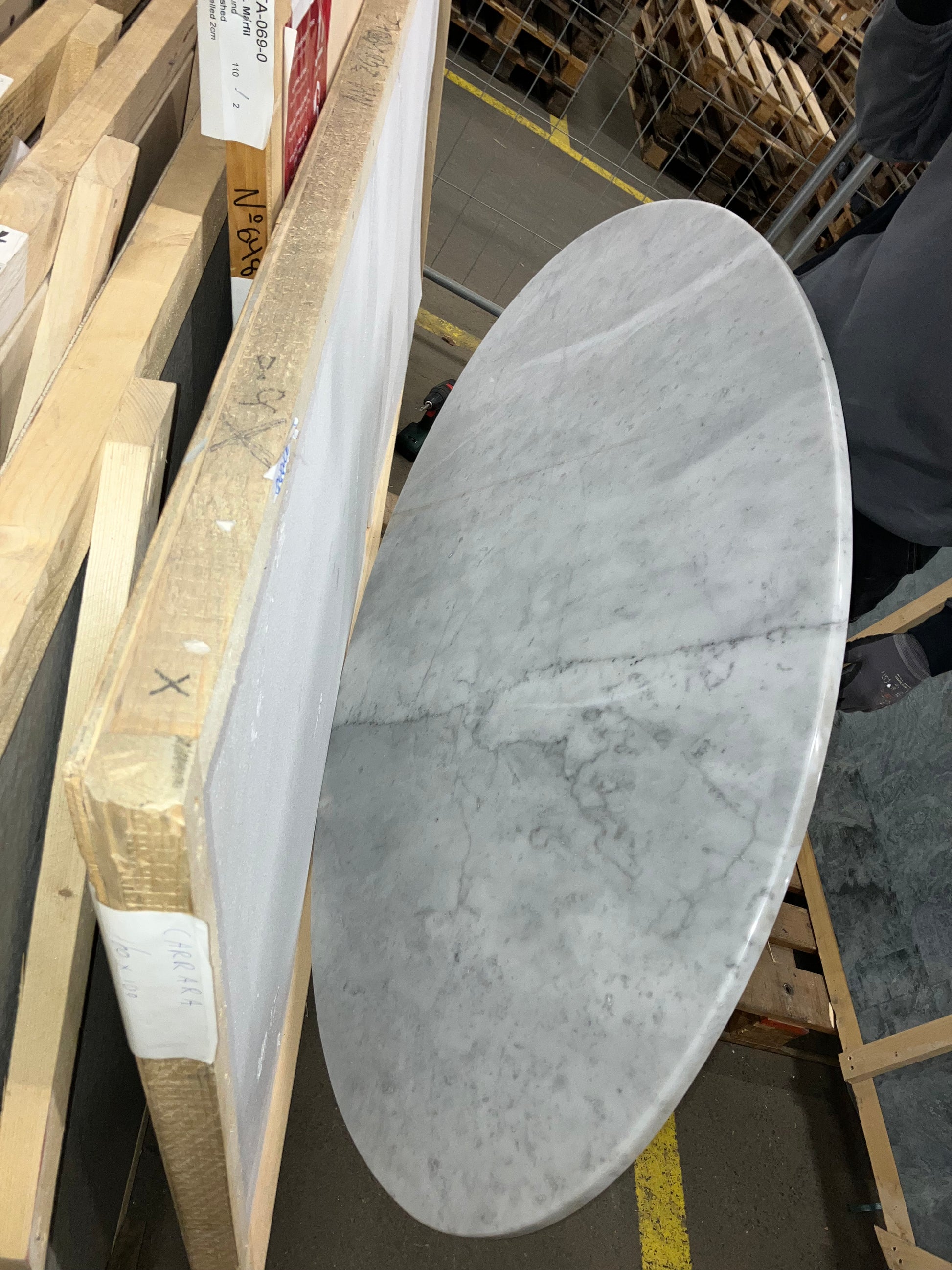 Oval marble dining table with Bianco Carrara white surface and cross-frame design, matte grey tint with small scratches.