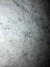 Rectangular marble dining table in Bianco Carrara White with four legs, matte finish, minor scratches visible in the image.