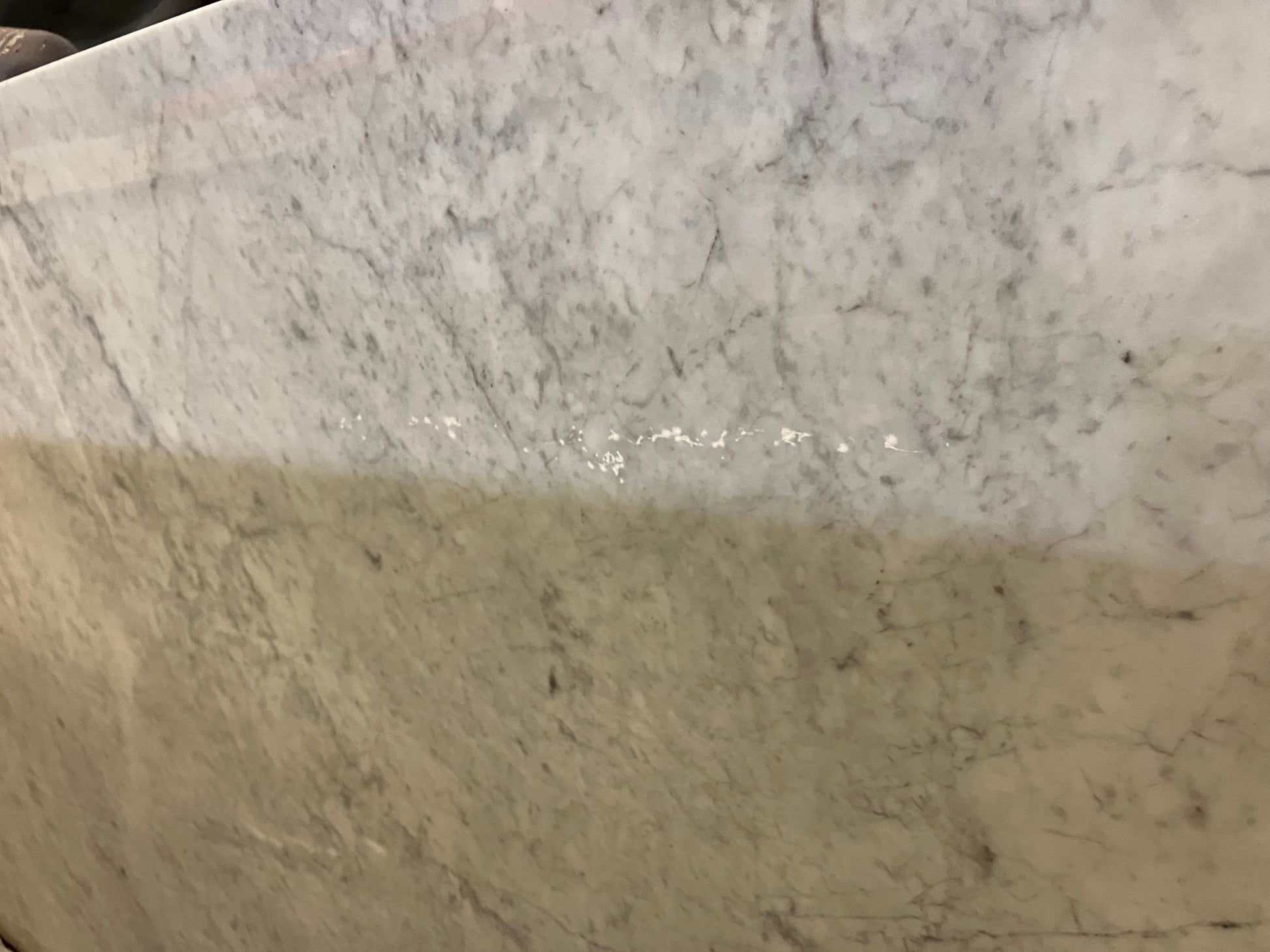 Rectangular marble dining table in Bianco Carrara white with four legs, matte finish, featuring light white streaks and spots.