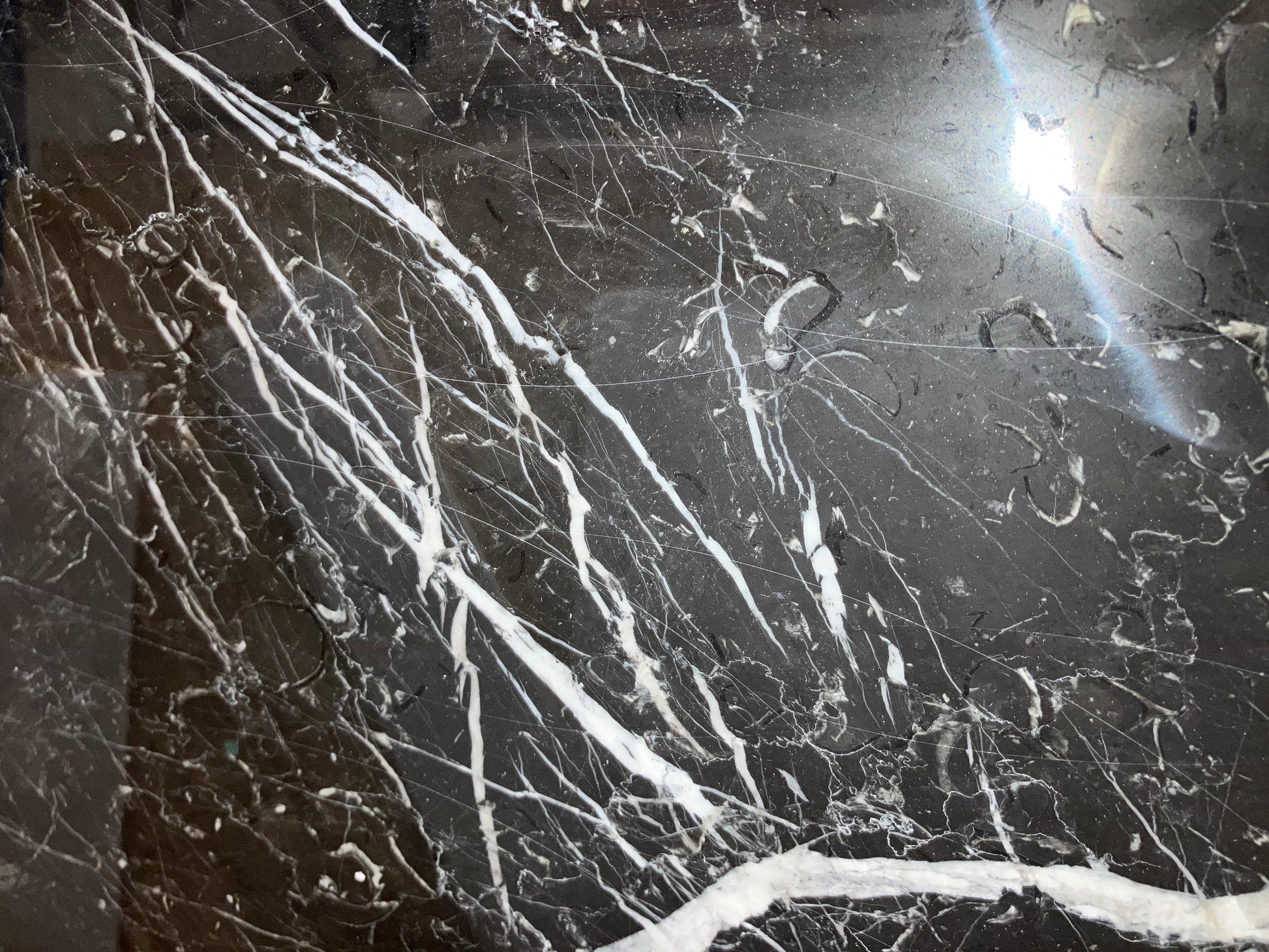 Rectangular Nero Marquina black marble dining table with U-frame base, glossy finish and visible scratches.