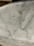 Round marble coffee table with Bianco Carrara white surface, matte finish, light brown spots, and subtle scratches.