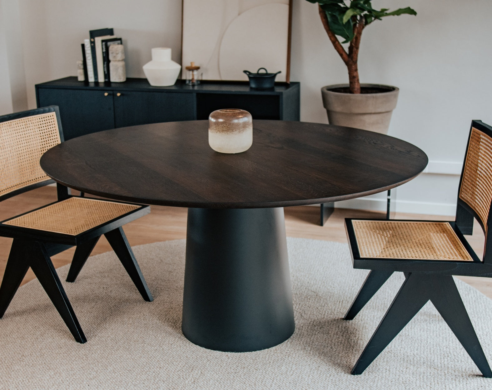 Flow round dining table in charcoal oak finish with black cylindrical base, featuring a sleek, modern design and subtle edge damage.