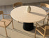 Flow round dining table in Ash White oak with black cylindrical base, slightly worn edge, 140 cm diameter, natural wood finish.