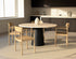 Flow round dining table in Ash White oak with black cylinder base, slightly worn edges and minor scratches, natural wood grain visible.