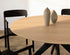 Round oak dining table with natural finish and arched frame, showcasing a smooth, circular surface and elegant wooden design.