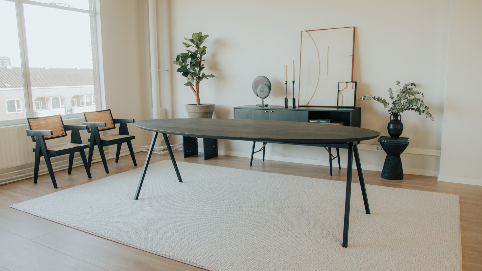 Oval oak dining table with charcoal finish and V-frame design, showcasing a sleek and modern dining surface.