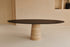 Oval FLOW dining table in smoked oak with travertine cylinder base, showcasing sleek modern design and natural wood finish.