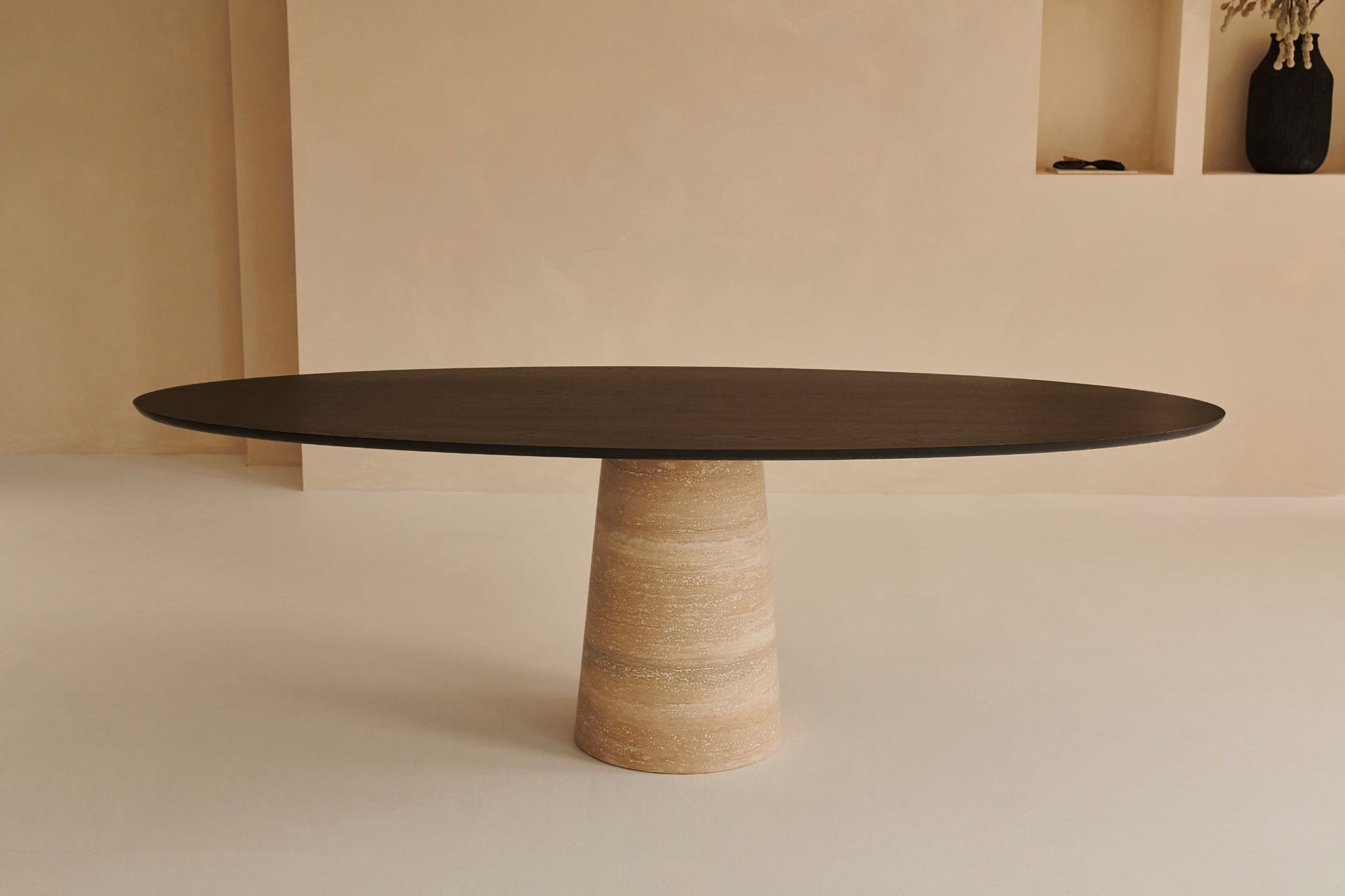 Oval FLOW dining table in smoked oak with travertine cylinder base, showcasing sleek modern design and natural wood finish.