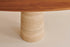 Oval walnut Flow dining table with travertin cylinder base, showing a sleek, modern wooden table with stone accents.