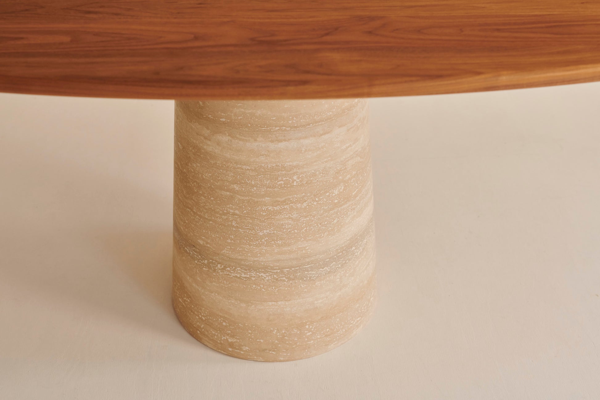 Oval walnut Flow dining table with travertin cylinder base, showing a sleek, modern wooden table with stone accents.