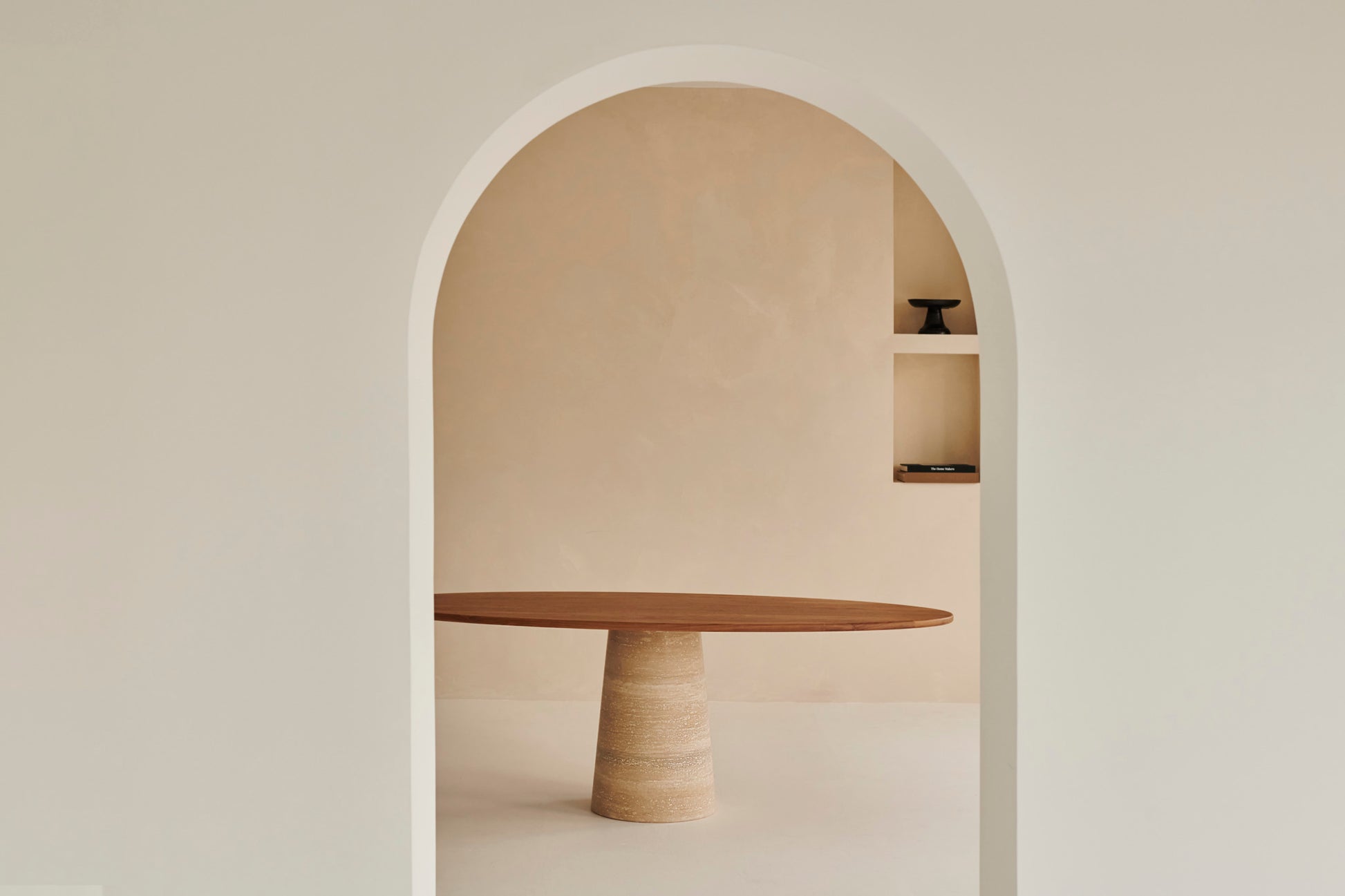 Oval walnut FLOW dining table with travertin cylinder base, featuring sleek modern design and natural wood finish.